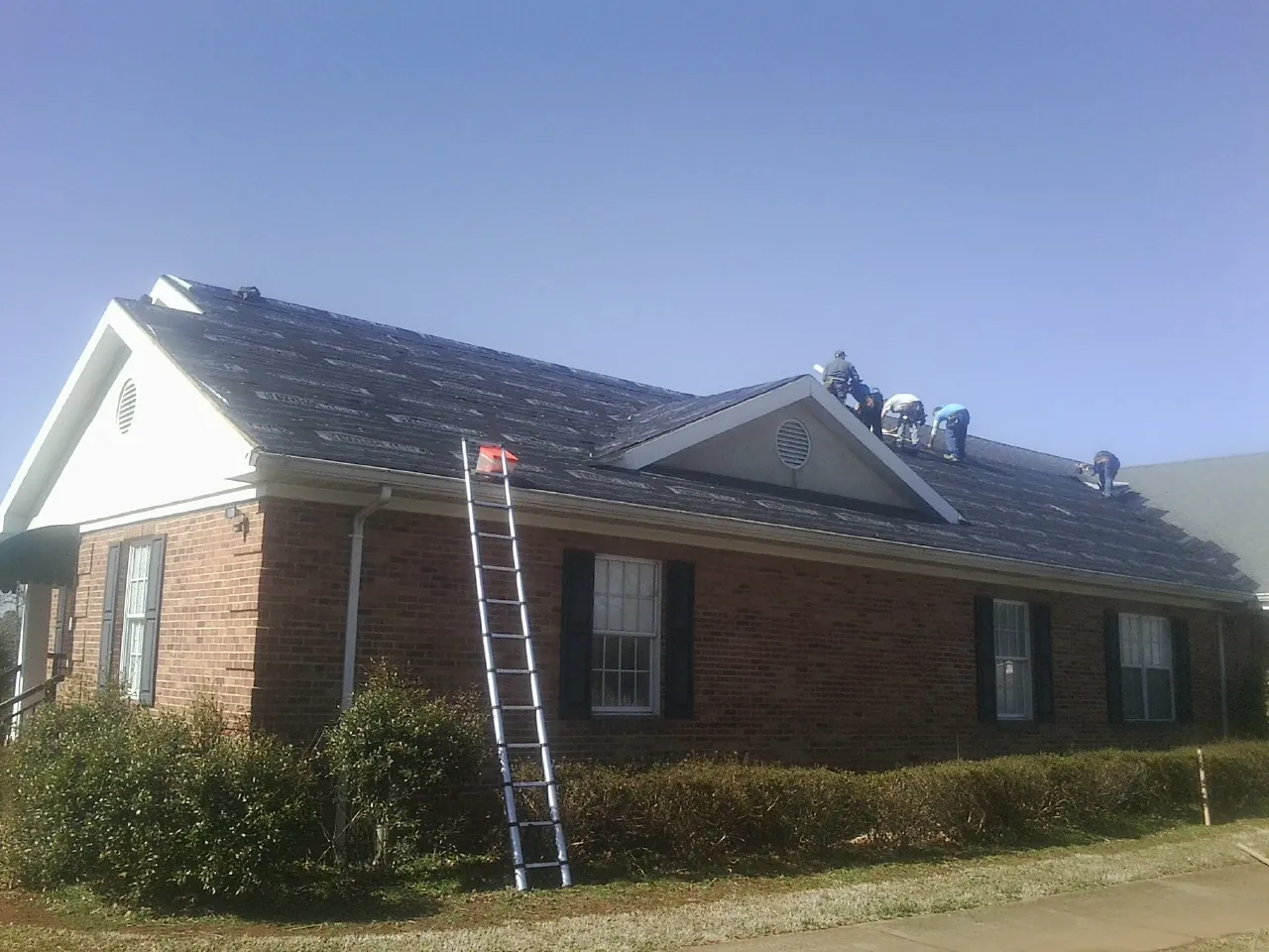 Crew tearing shingles off a brick ranch roof with a ladder set — Metal Roof Repair work by our crew in Scotrun