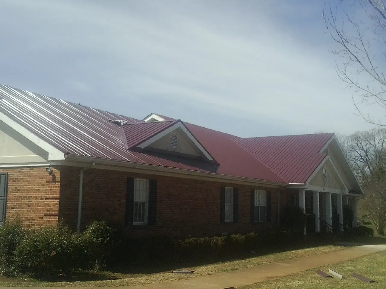 Red metal roof with gabled entries on a long brick building, from a Hail Damage Roof Repair job in Scotrun