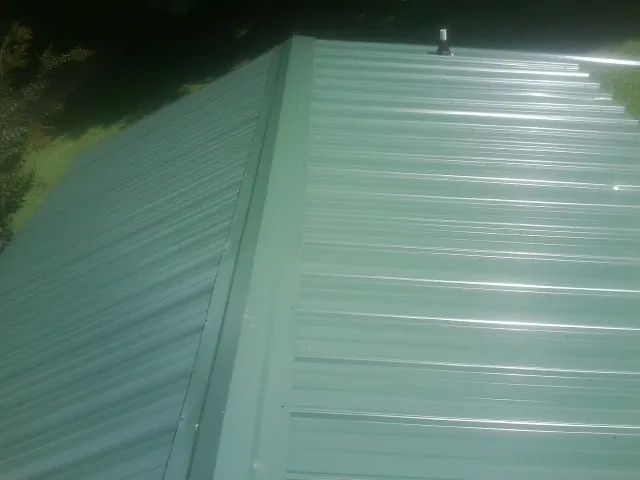 New green metal panels meeting at the ridge of a roof — Flat Roof Repair work by our crew in Scotrun