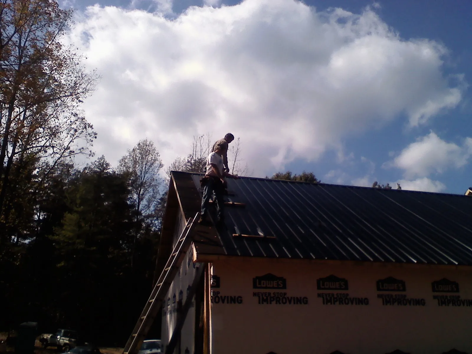 Roofer fastening dark metal panels high against a cloudy sky, from a Roof Inspection job in Scotrun