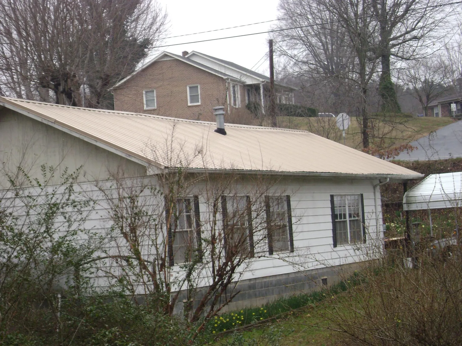 Tan metal roof on a white sided house set into a hillside — Commercial Roofing by Roofing Brothers in Scotrun